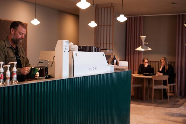 kvinde staar med en kop kaffe kigger ind i kameraet og smiler