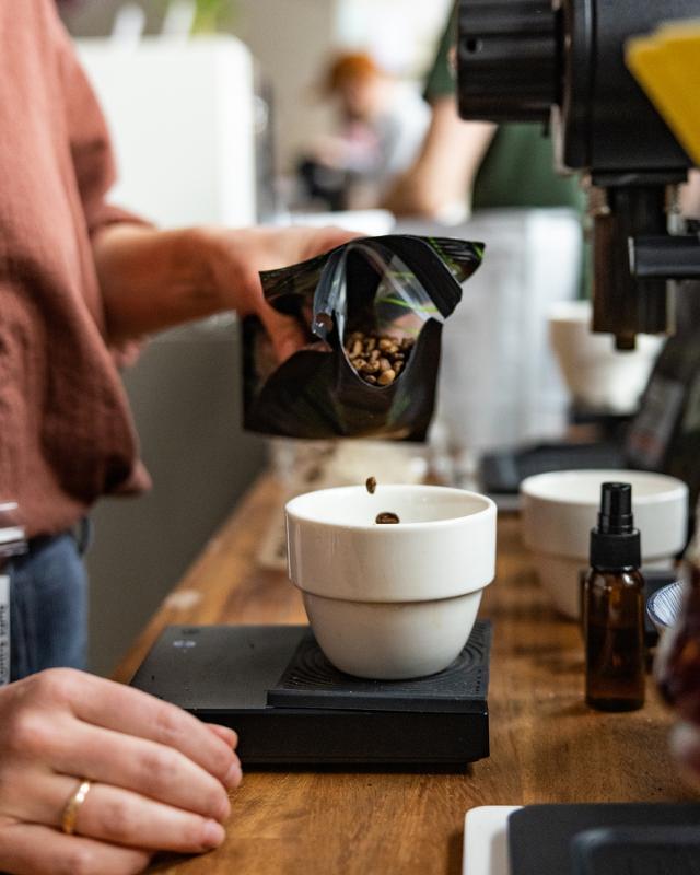 Pige haelder kaffeboenner ned i en lille skaal der staar paa en kaffevaegt