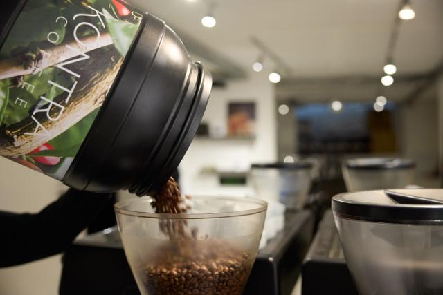 moerkristede kaffeboenner haeldes fra en kaffetoende ned i en kaffekvaern