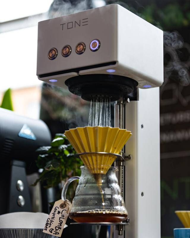 tone kaffermaskine brygger pourover kaffe i en gul origami tragt over en hario glaskande