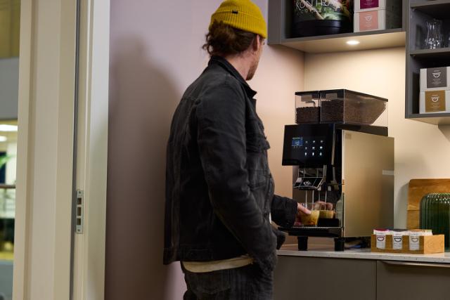 person henter kaffe ved kaffemaskine med indbygget kaffekvaern