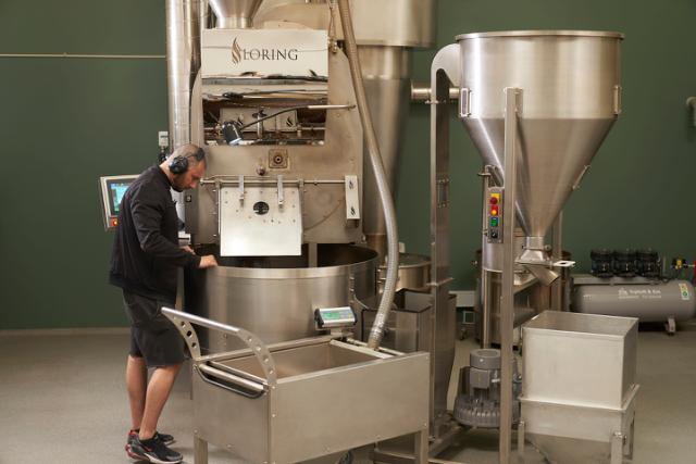 ristemester staar ved kafferister og kigger paa kaffeboennerne der koeler af