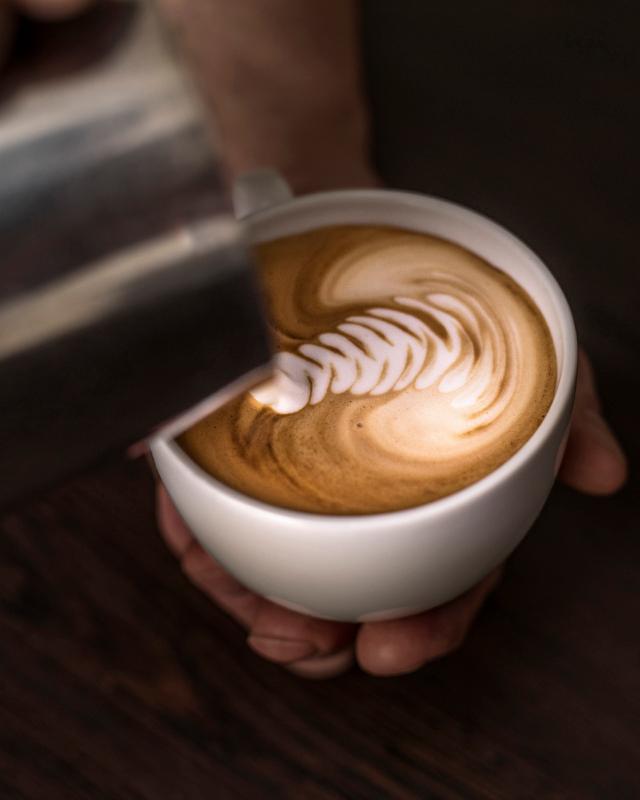 ophaeldning af smuk latteart haand holder kaffekop maelk haeldes fra kande