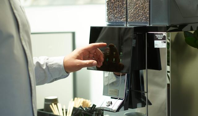 person vaelger kaffe paa en touchskaerm paa en fuldautomatisk kaffemaskine